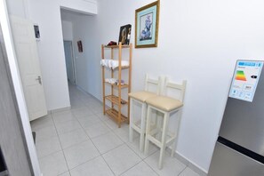 A hallway with a white door, a wooden shelf with towels, a framed picture, and a refrigerator with a control panel. - Soothing 2-bedroom apartment with AC in charming Mont Choisy near Golf&sea (Grand Baie)