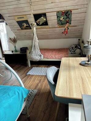 Une pièce chaleureuse avec un lit, un fauteuil suspendu en macramé, une petite table et un bureau.