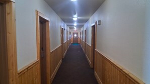 Un largo y estrecho pasillo con paneles de madera en las paredes y piso alfombrado, que conduce a una puerta al final.