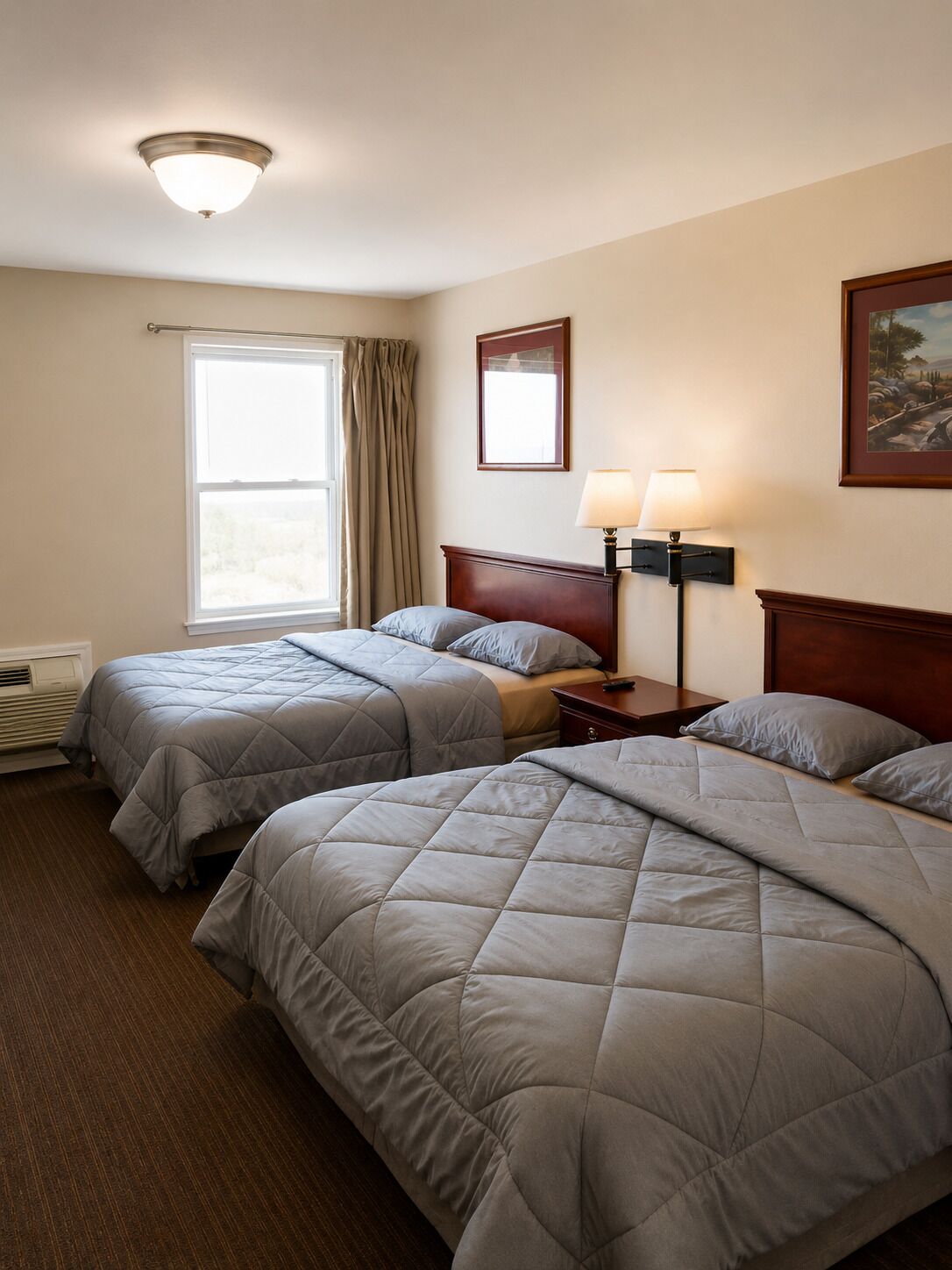 Une chambre d’hôtel avec deux lits, une fenêtre avec des rideaux, une lampe fixée au mur et un tableau.