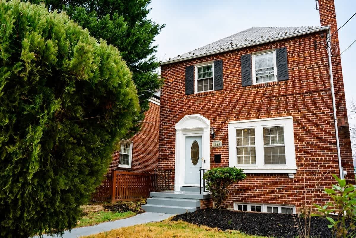 A two-story brick house with a white front door, a small porch, and a mailbox.