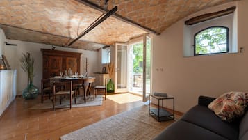 A spacious living area with a brick ceiling, a dining table set with chairs, a sofa, and a window with a view of greenery.