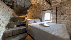 Ein Schlafzimmer mit Steinwänden, einem Bett, einem Fenster und einer Treppe.