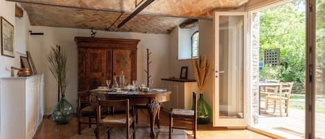 A dining area with a brick ceiling, a wooden table set for four, and a view of the garden through an open door.
