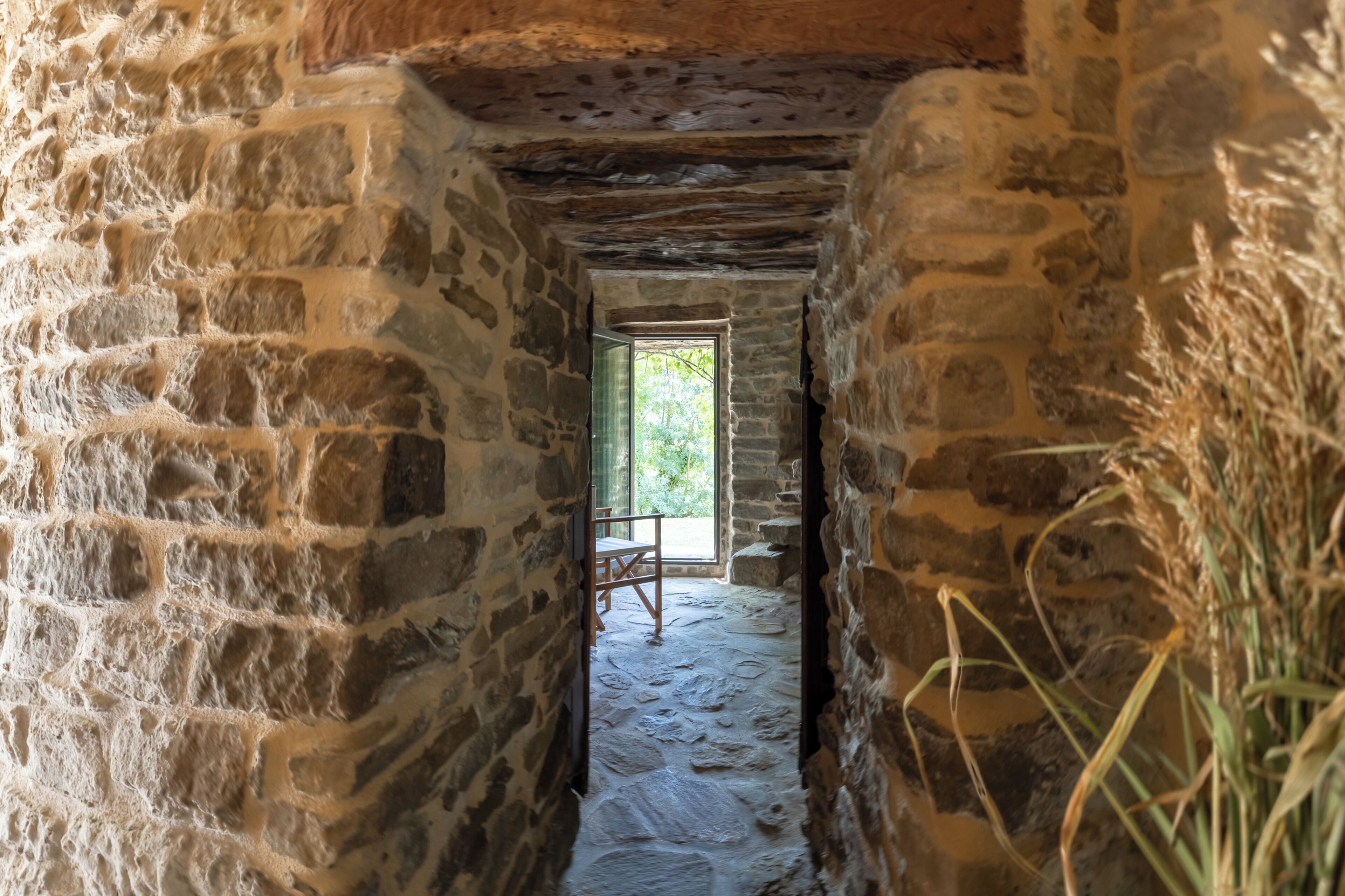 Un couloir en pierre avec une chaise en bois et une fenêtre donnant sur un espace extérieur.
