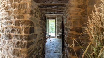 Un couloir en pierre avec une chaise en bois et une fenêtre donnant sur un espace extérieur.