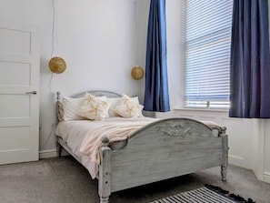 A bedroom with a bed, a door, a window with blinds, and a wall-mounted light fixture. - Jurassic coast spacious and stylish 2 bed 2 bath apartment. With own parking. (Portland)