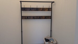Un banco de metal con una cesta trenzada debajo, un perchero en la pared y un letrero de bienvenida.