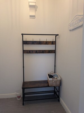 A metal bench with a woven basket underneath, a wall-mounted coat rack, and a welcome sign. - Jurassic coast spacious and stylish 2 bed 2 bath apartment. With own parking. (Portland)