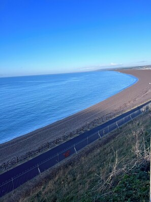 A coastal road with a metal fence, a pebble beach, and the ocean. - Jurassic coast spacious and stylish 2 bed 2 bath apartment. With own parking. (Portland)
