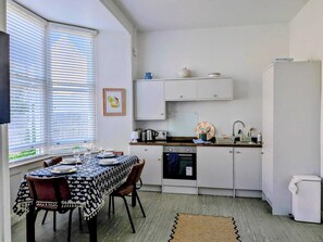 A compact kitchen with white cabinets, a dining table set for four, and a window with blinds. - Jurassic coast spacious and stylish 2 bed 2 bath apartment. With own parking. (Portland)