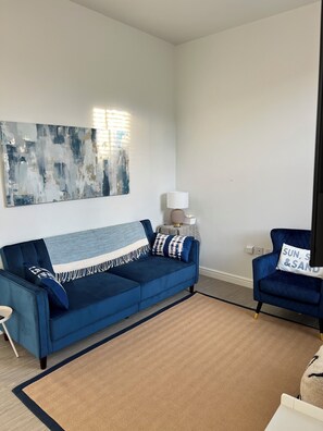Un salon avec un canapé bleu, un fauteuil bleu, un tapis, une lampe et une œuvre d’art murale.