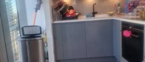 Eine moderne Küche mit grauen Schränken, einer Edelstahl-Mülltonne und einem kleinen Fenster.