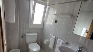 A modern bathroom with a toilet, bidet, sink, and a window.