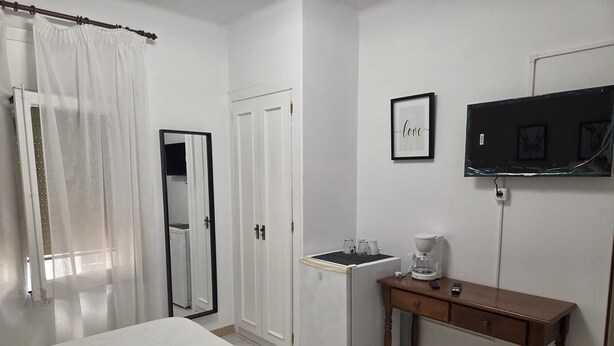 Ein Hotelzimmer mit einem Bett, einem kleinen Tisch mit einer Kaffeemaschine, einem an der Wand befestigten Fernseher und einem gerahmten Bild mit dem Wort 'love'.