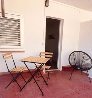 A patio with a wooden table and chairs, a black woven chair, and a window with blinds.
