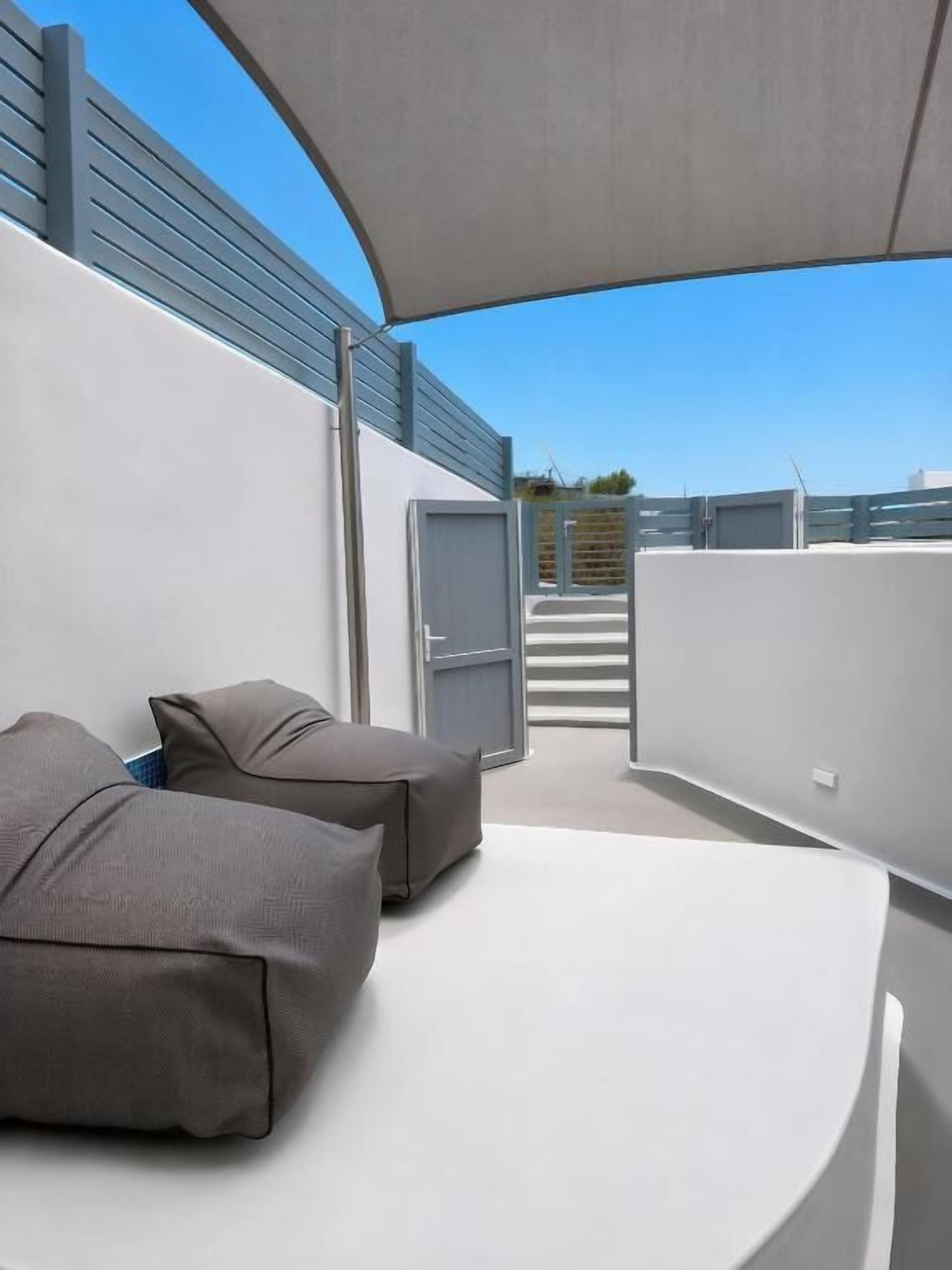 A modern outdoor seating area with a curved white bench and grey cushions, a covered walkway, and a view of the cityscape.