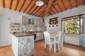 A kitchen with a tiled backsplash, wooden ceiling beams, a dining table with chairs, and a window with a view of greenery. - Casa al Poggio. An 18th-century farmhouse in the Val d'Orcia. Perfect for families (Castiglione d'Orcia)