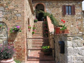 A stone building with a staircase leading to an entrance, surrounded by potted plants and flowers. - Casa al Poggio. An 18th-century farmhouse in Val d'Orcia. Perfect for families (Castiglione d'Orcia)