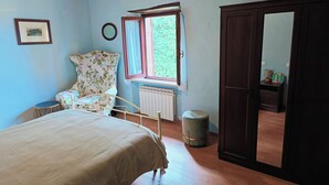 Makuuhuoneessa on sänky, tuoli, ikkuna, patteri, ovi ja pieni jakkara.