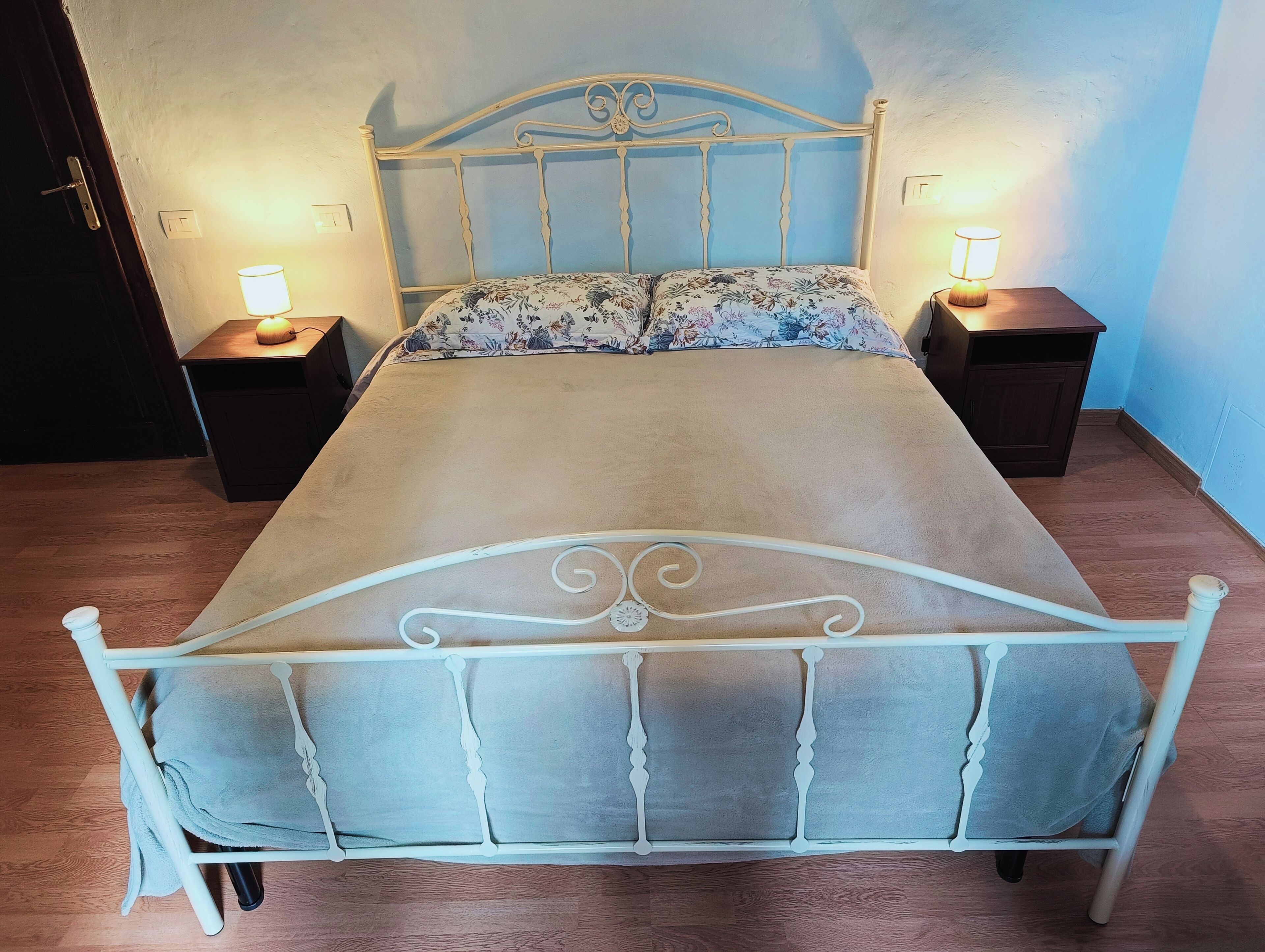 A bed with a metal frame and a floral bedspread, flanked by two bedside tables with lamps.