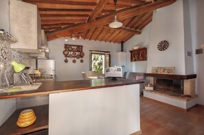 A kitchen with a wooden ceiling, a built-in stove, a dining area with a table and chairs, and a fireplace. - Casa al Poggio. An 18th-century farmhouse in Val d'Orcia. Perfect for families (Castiglione d'Orcia)