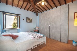 Un dormitorio con cama, ventana, ventilador de techo, armario y un cuadro en la pared.