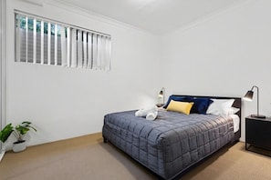 Ein Schlafzimmer mit einem Bett, einem Nachttisch, einer Lampe und Topfpflanzen.