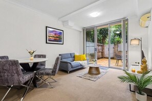 A modern living room with a sofa, chairs, a coffee table, and a dining area. - Apartment - Ground Floor Sydney (Parramatta)