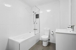 Ein modernes Badezimmer mit einer gläsernen Duschkabine, einer weißen Badewanne, einer Toilette und einem Waschbecken mit Spiegel.
