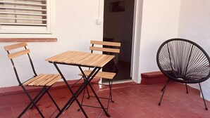 Un pati amb una taula i cadires de fusta, una cadira negra de fibra i una finestra amb persianes.