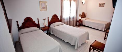 A hotel room with two single beds, a small table, a chair, and a window with curtains.