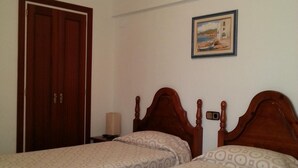 Una habitació amb dos llits individuals, un armari de fusta, un quadre a la paret i una taula de nit amb una làmpada.