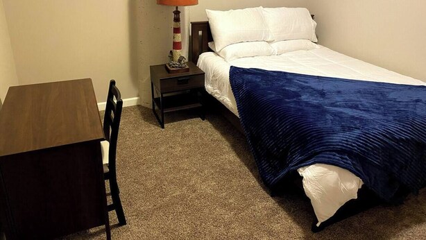 A small, neatly arranged bedroom with a single bed, a nightstand, a table, and a lamp. - Waterfront patio 2 bedroom condo (Sandusky)