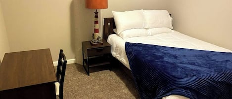 Un dormitorio pequeño y ordenado con una cama individual, una mesita de noche, una mesa y una lámpara.