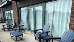 A patio with Adirondack chairs and a small table, a glass door entrance, and a brick wall. - Waterfront patio 2 bedroom condo (Sandusky)