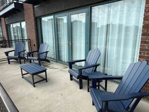 Um pátio com cadeiras Adirondack e uma mesa pequena, porta de vidro e parede de tijolos.