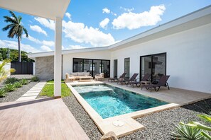 A modern outdoor pool area with a clear blue pool, lounge chairs, and a seating area with a table and chairs. - 3BR Surfside Home with Large Pool & BBQ (Playa Potrero)