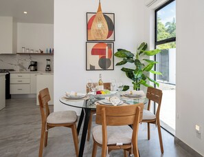 A modern dining area with a glass table, wooden chairs, and a large plant. - 3BR Surfside Home with Large Pool & BBQ (Playa Potrero)