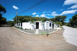 A single-story building with a front entrance, surrounded by gravel and small plants. - 3BR Surfside Home with Large Pool & BBQ (Playa Potrero)
