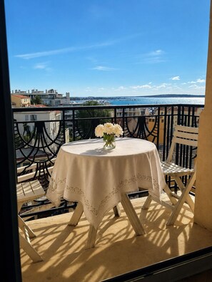 A balcony with a round table and chairs, a vase with flowers, and a view of the sea and buildings. - Charming 2-bedroom apartment with AC in beautiful Cannes (Cannes)