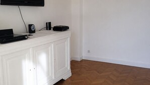 Ein Zimmer mit einem weißen Schrank, einem wandmontierten Flachbildfernseher und einem Holzboden mit Fischgrätmuster.