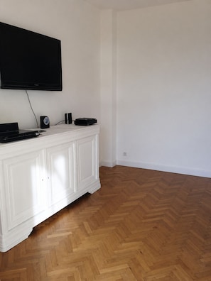 A room with a white cabinet, a flat-screen TV mounted on the wall, and a herringbone-patterned wooden floor. - Charming 2-bedroom apartment with AC in beautiful Cannes (Cannes)