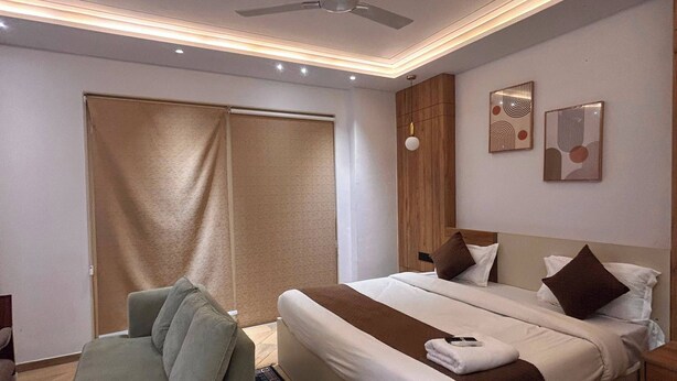 A modern hotel room with a bed, a sofa, a ceiling fan, and artwork on the walls. - Hotel alvish (New Delhi)