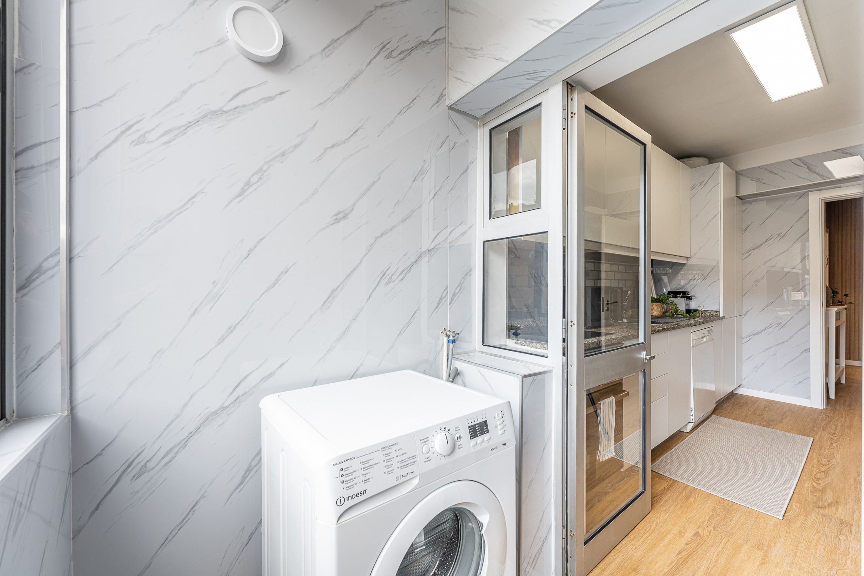 A modern kitchen with a built-in washing machine, marble walls, and a wooden floor.