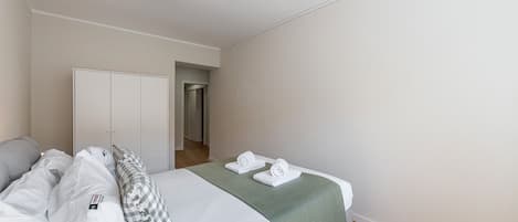 Une chambre d’hôtel avec un lit, une couverture verte et une serviette blanche.