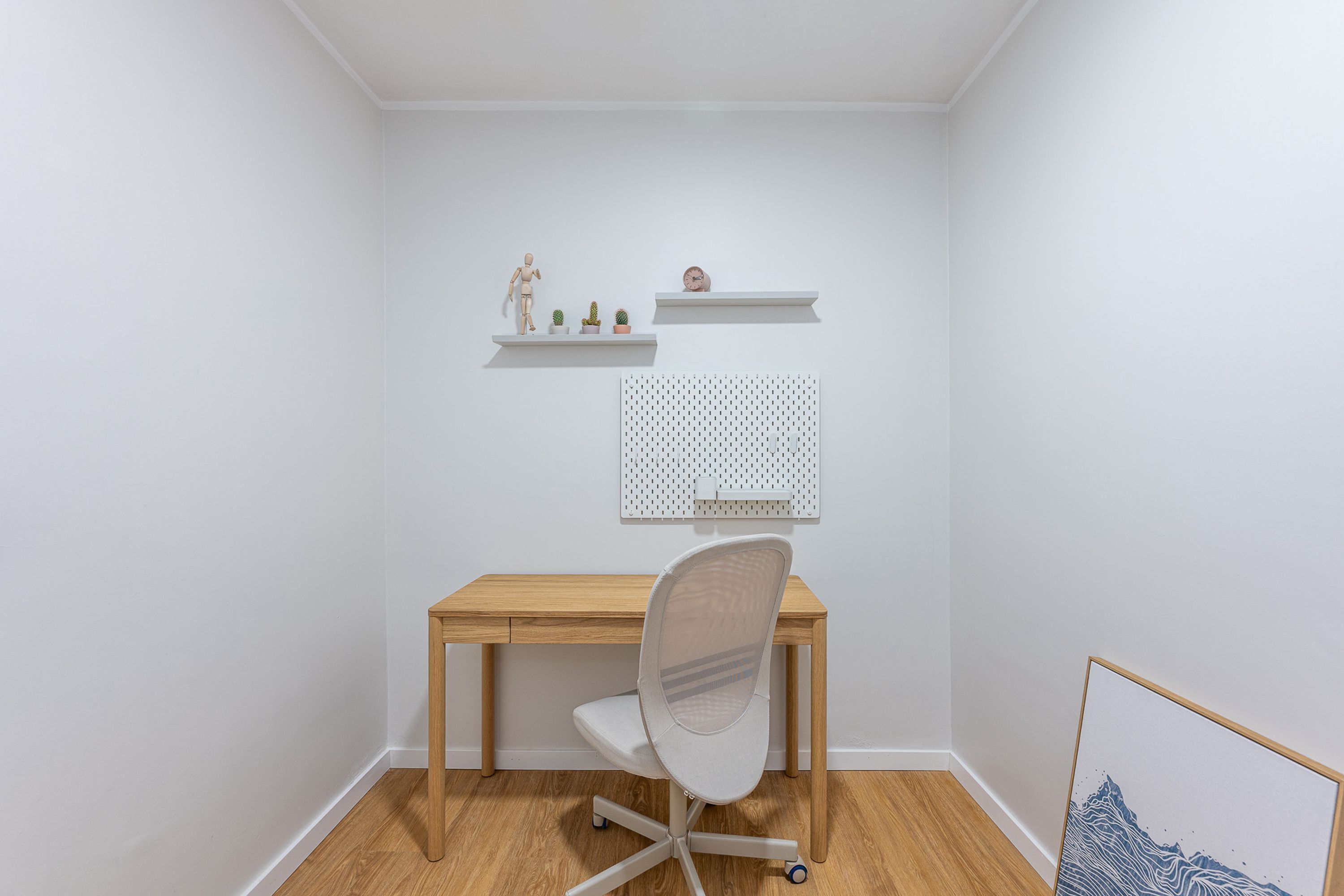 A small, neatly organized room with a wooden desk, a white chair, and two white shelves with decorative items.