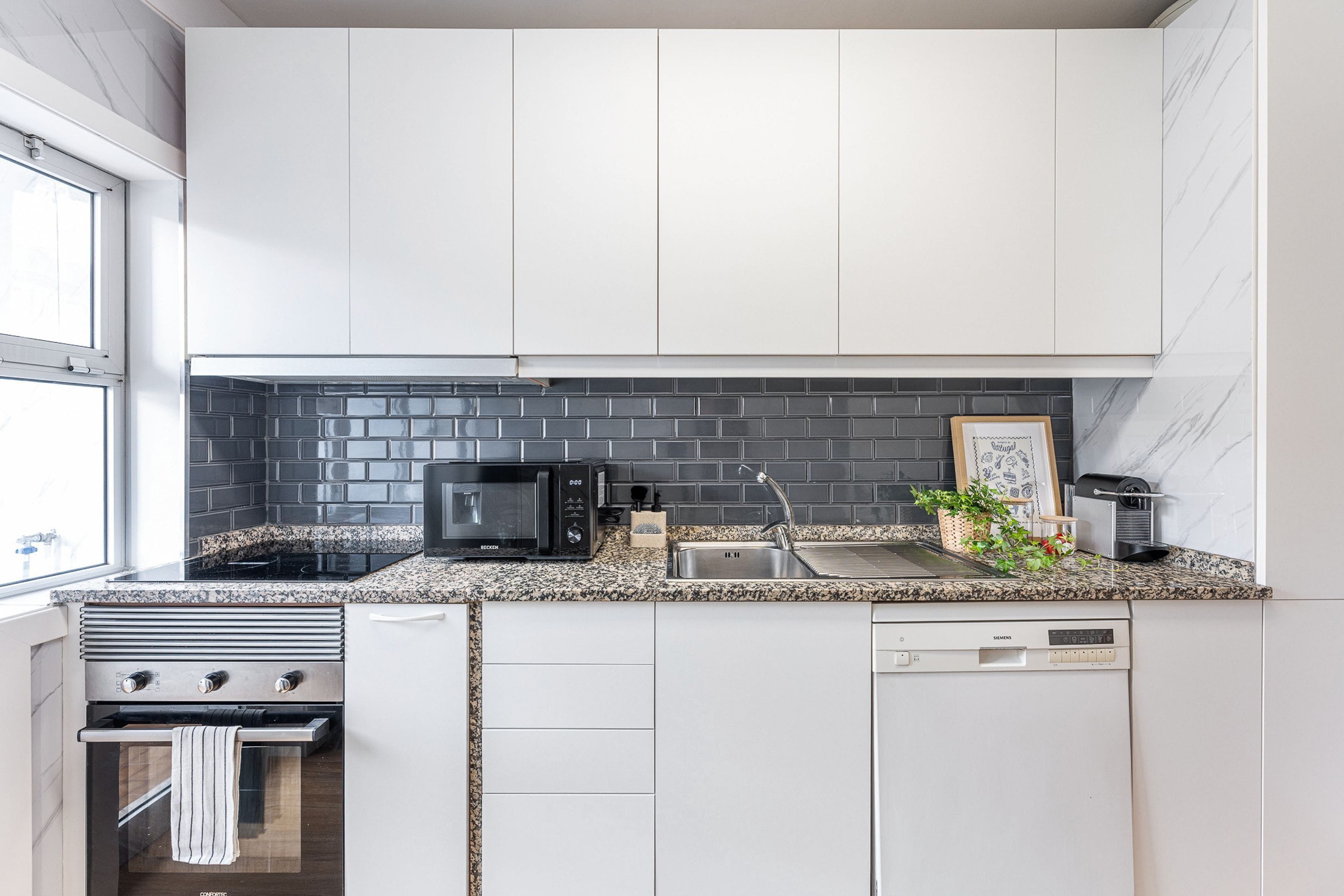 A modern kitchen with white cabinets, a black tiled backsplash, a microwave, a sink, and a dishwasher.