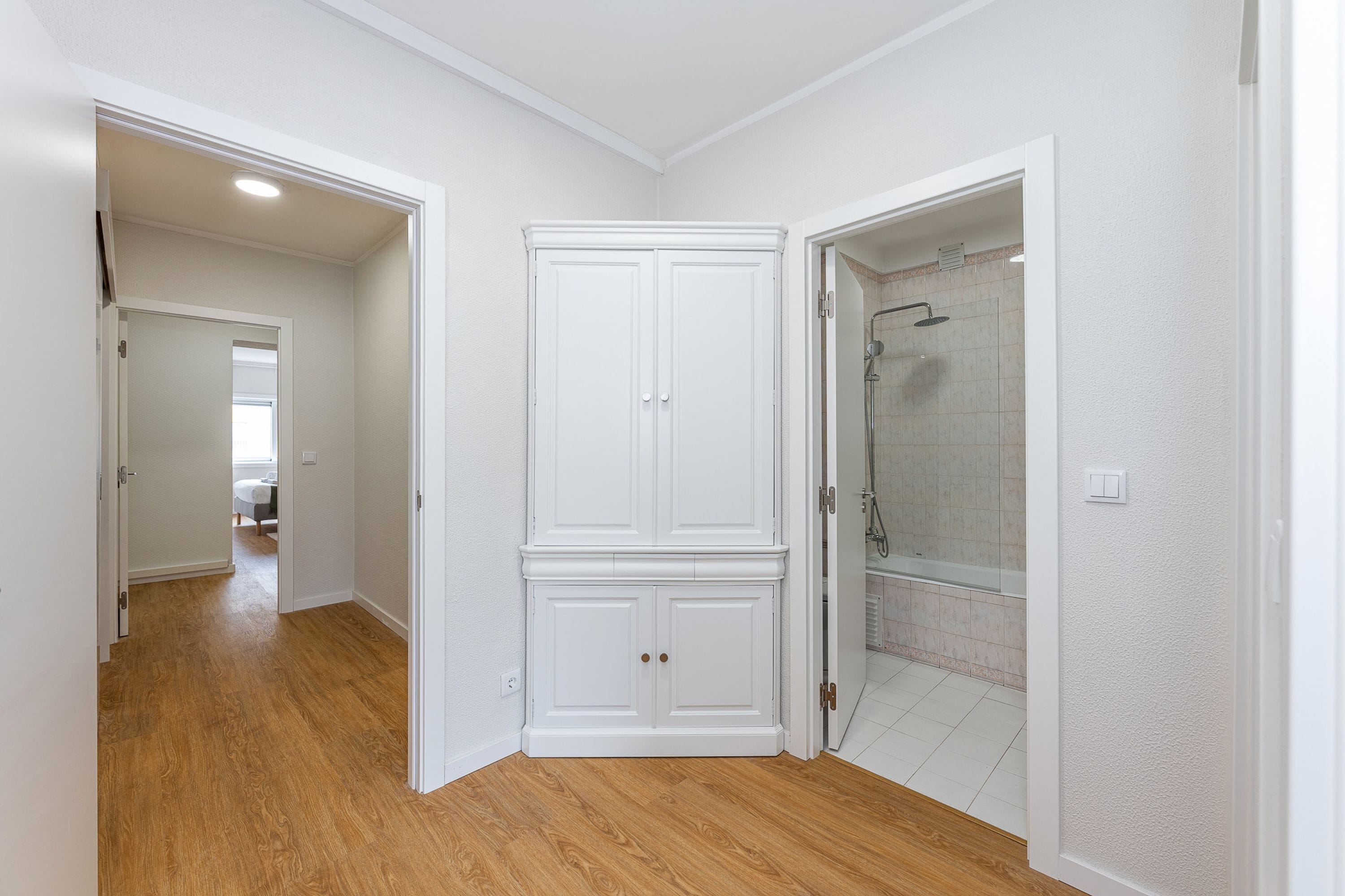 A hallway with wooden flooring, a white wardrobe, and a shower area with tiled walls.