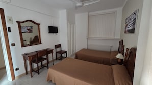 Ein Schlafzimmer mit zwei Betten, einem Schreibtisch, einem Stuhl, einem Fernseher und einem Deckenventilator.